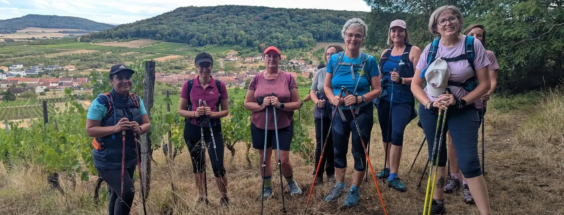 Le groupe de l’association, bâtons en main, sur un chemin des coteaux ; la côte boisée ferme l’horizon.