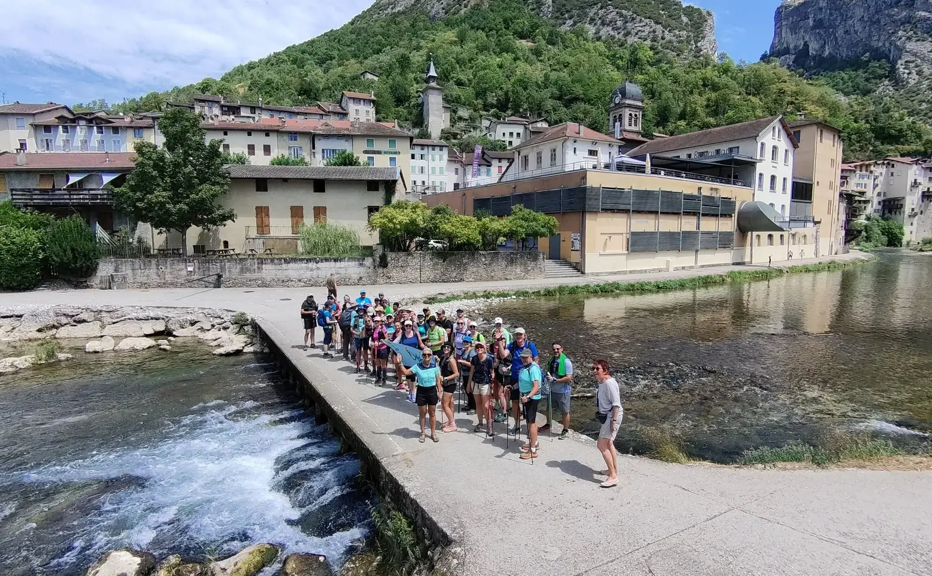 Le groupe de l’association traverse un seuil de pierre, un village au bord de l’eau derrière.